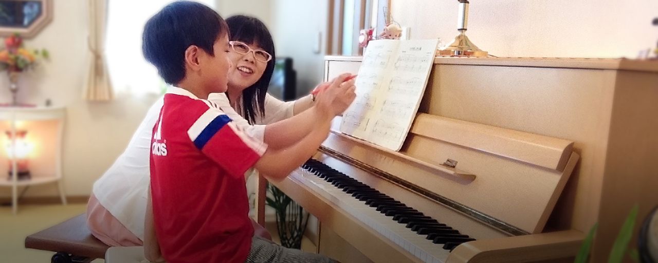 アイキャッチ画像：楽譜を広げてピアノの前に座っている笑顔の男の子と、指導している講師