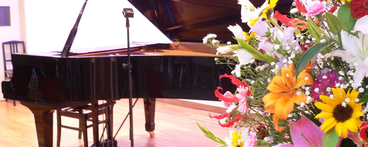 アイキャッチ画像：大きなスタンド花越しに見えるステージ上のグランドピアノ