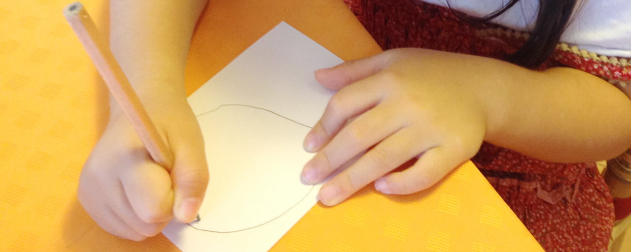サムネイル画像：テーブルの上でメモ用紙に鉛筆で丸い円を描く小さな女の子の手元の写真