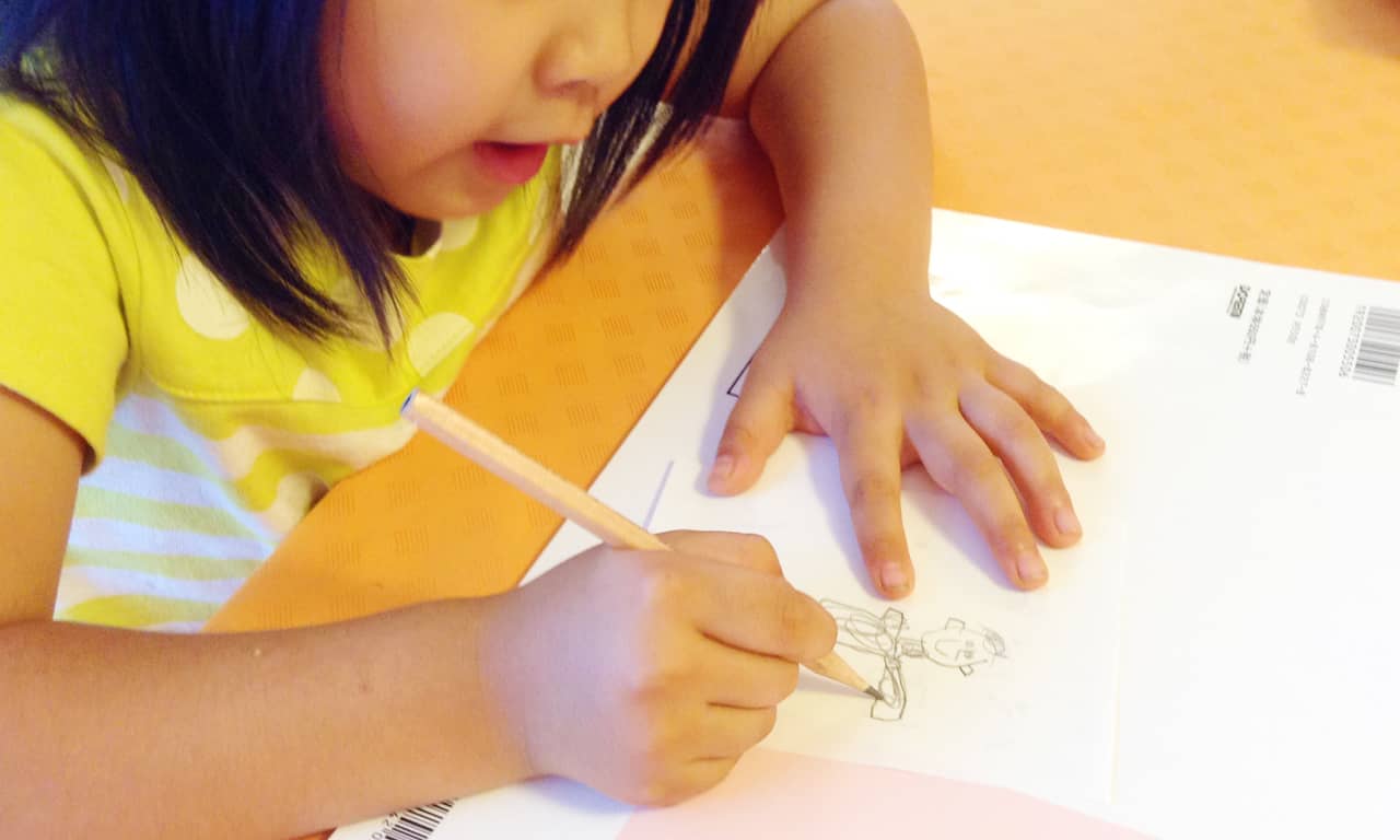 写真:ワークブックの上に置いた紙に、パパに似ている男性の絵を描く女の子