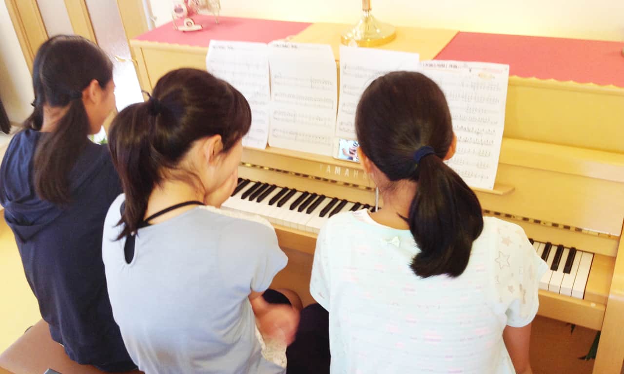 写真:三人での連弾の練習の様子を動画で撮影して、スマホで確認している女の子たち