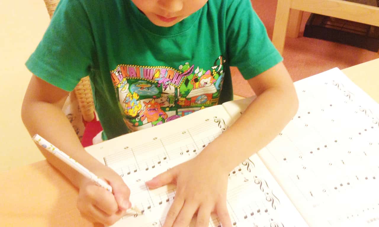 写真:ワークブックの五線譜に、指番号を書き込んでいく男の子