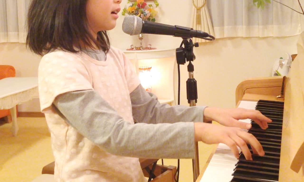 写真:マイクを立てて、ピアノの弾き語りを練習する女の子