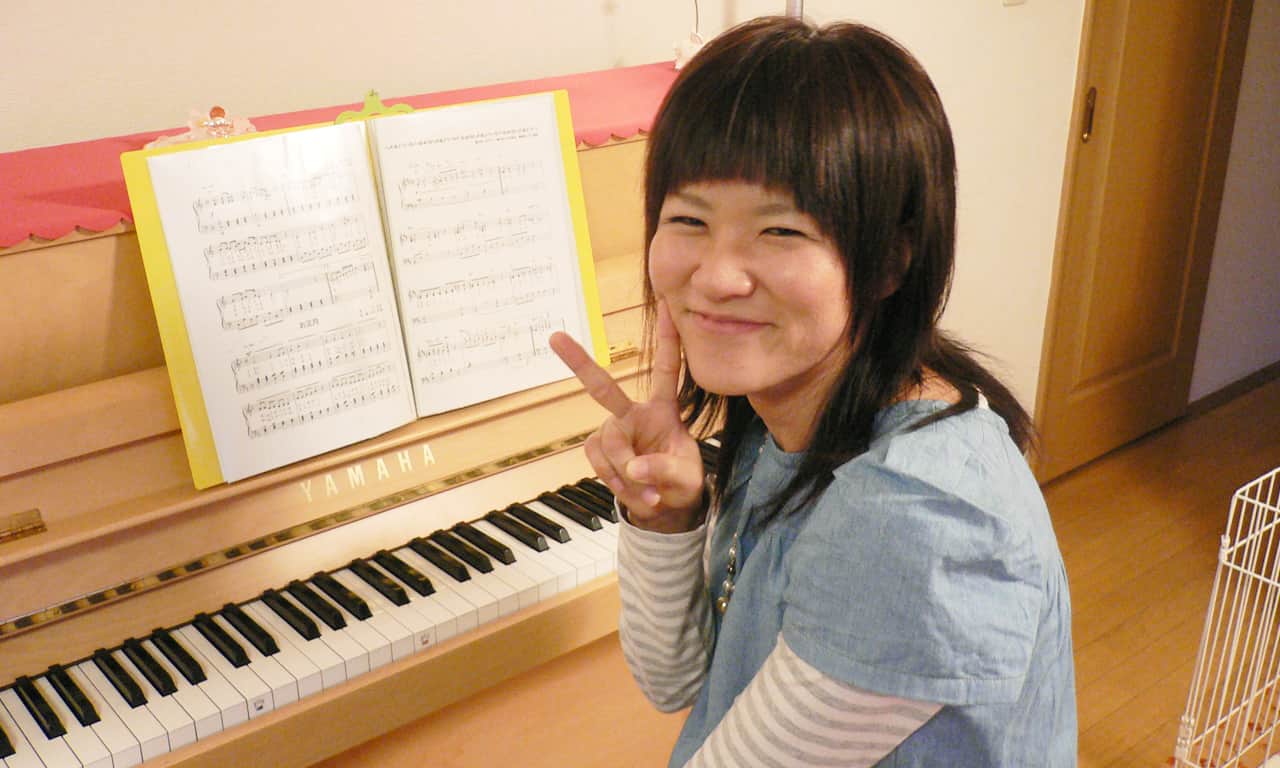 写真:ピアノの前でピースサインの山本亜紀様