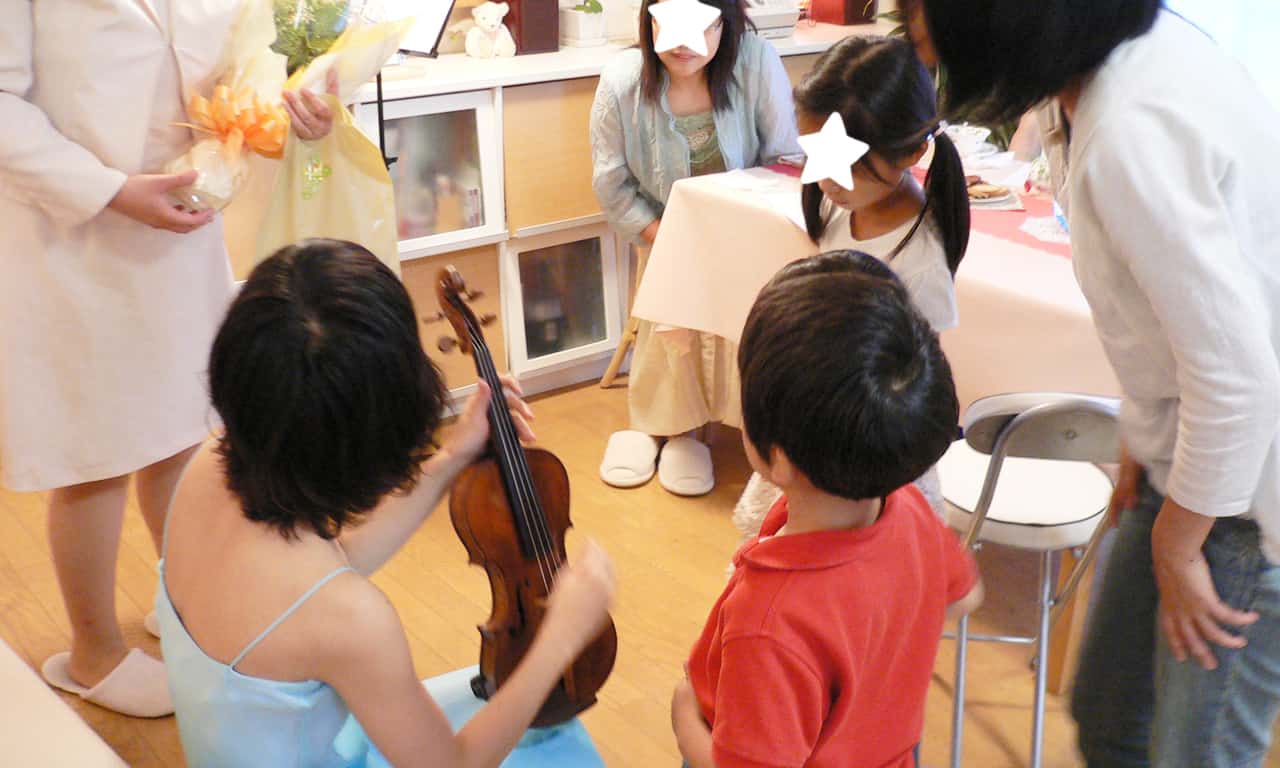 写真：生徒さんたちに囲まれて、ヴァイオリンの説明をしている進藤瑞希さん