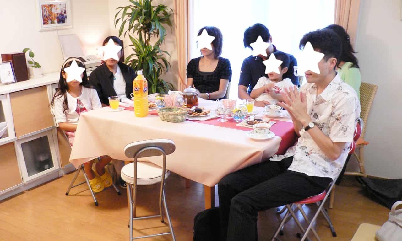 写真：飲み物とお菓子が並んだテーブルで、チェロの演奏を楽しんでいる生徒さんたち