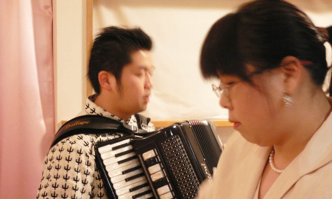 写真：アコーディオンを弾く田ノ岡三郎さんと、ピアノを弾く講師のアップ