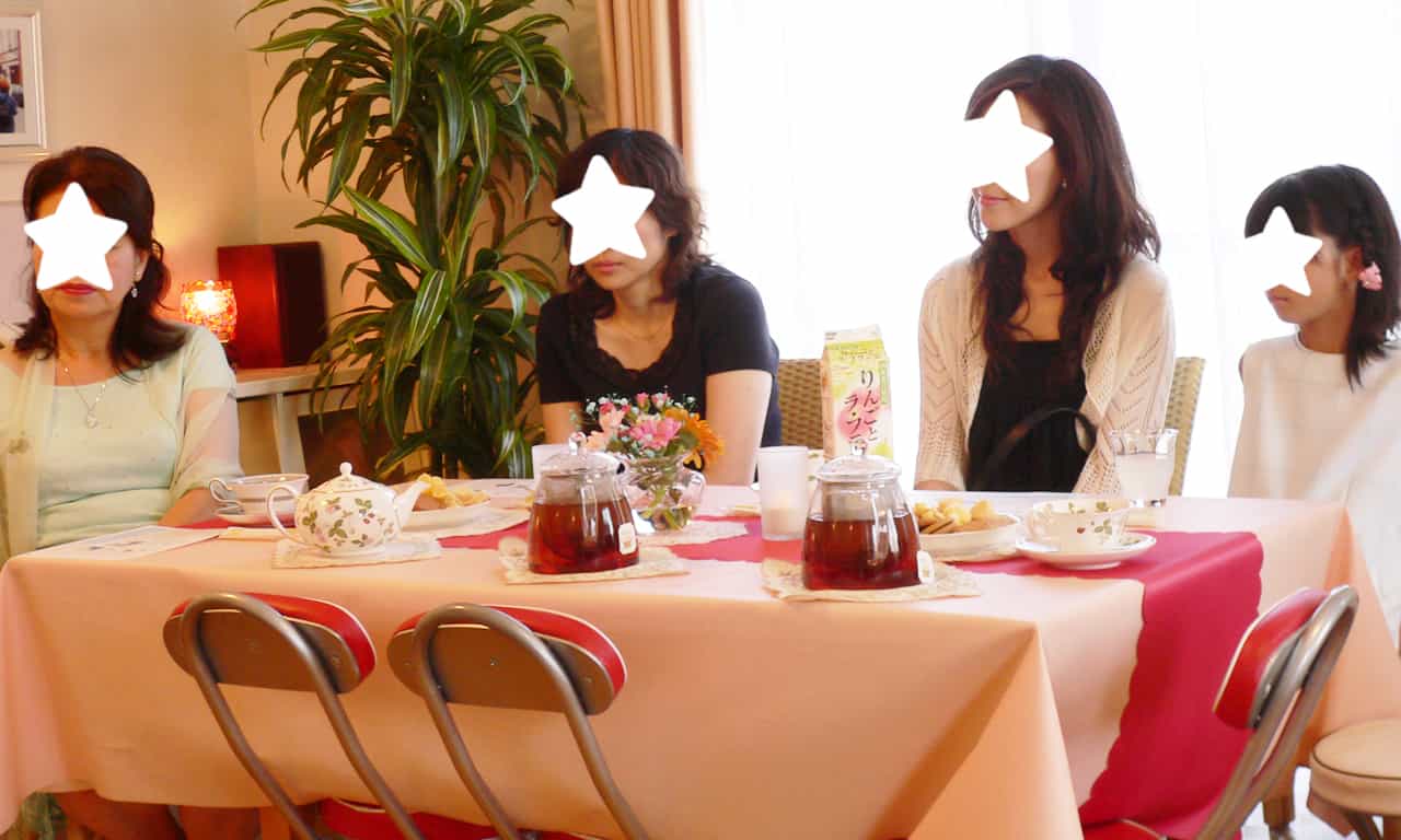 写真：紅茶とお菓子が並んだテーブル席で演奏に聴き入る生徒さんたち