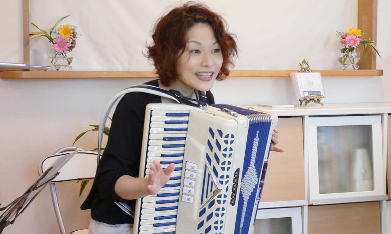 写真：アコーディオンを抱えたまま、身振り手振りを交えて話しているマルカートさん