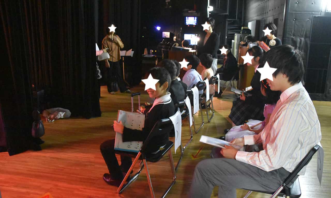 写真：ステージ脇に並べられたイスに座って、自分の出番まで待っている10名ほどの子どもたち