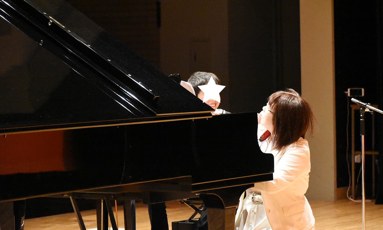 写真：ピアノの前で笑顔を浮かべて講師を見ている男の子