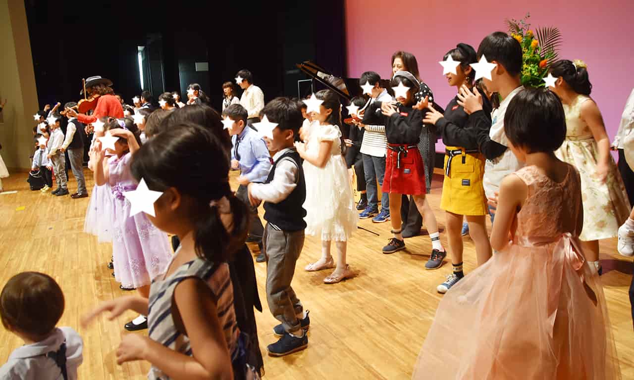 写真：ステージ上にたくさんの子どもたちが集い、楽しく歌ったり踊ったり、楽器を演奏したりしている様子