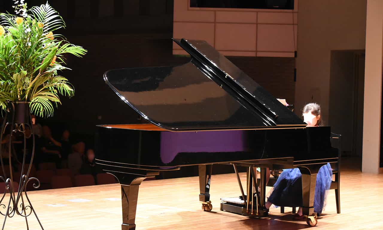 写真：ピアノ・ソロで演奏している紺色のドレスを着た女の子