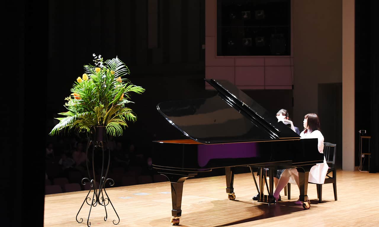 写真：ピアノ連弾をしている学校の制服を着た女の子と講師