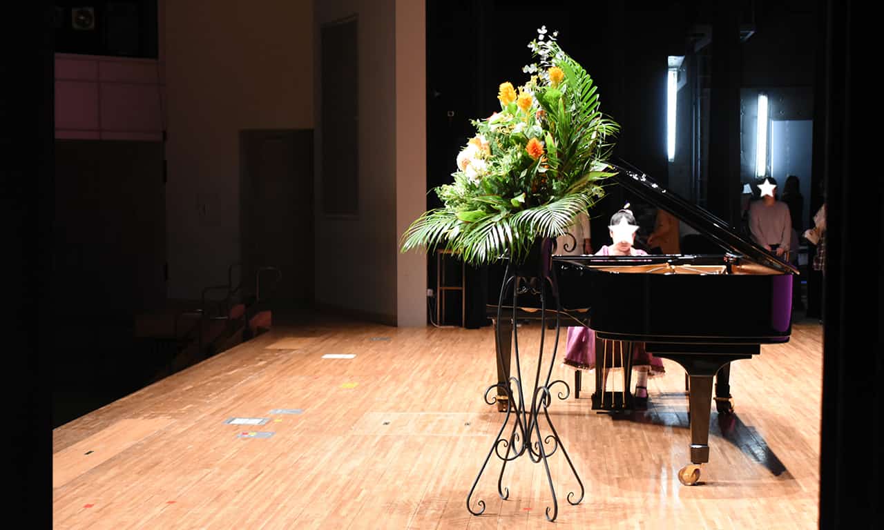 写真：広いステージで大きなピアノを弾いている、紫色のドレスを着た女の子