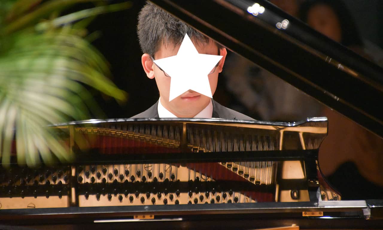 写真：ひとりでピアノを弾いている高校生の男の子を正面から捉えた様子