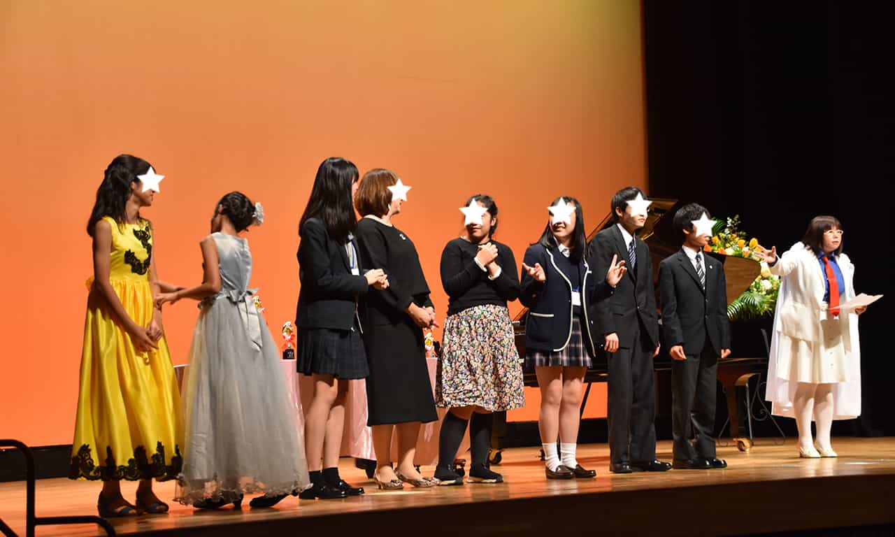 写真：ステージで横並びに並んだ8名のオーディエンス賞受賞者のみなさんと、その横で説明している講師