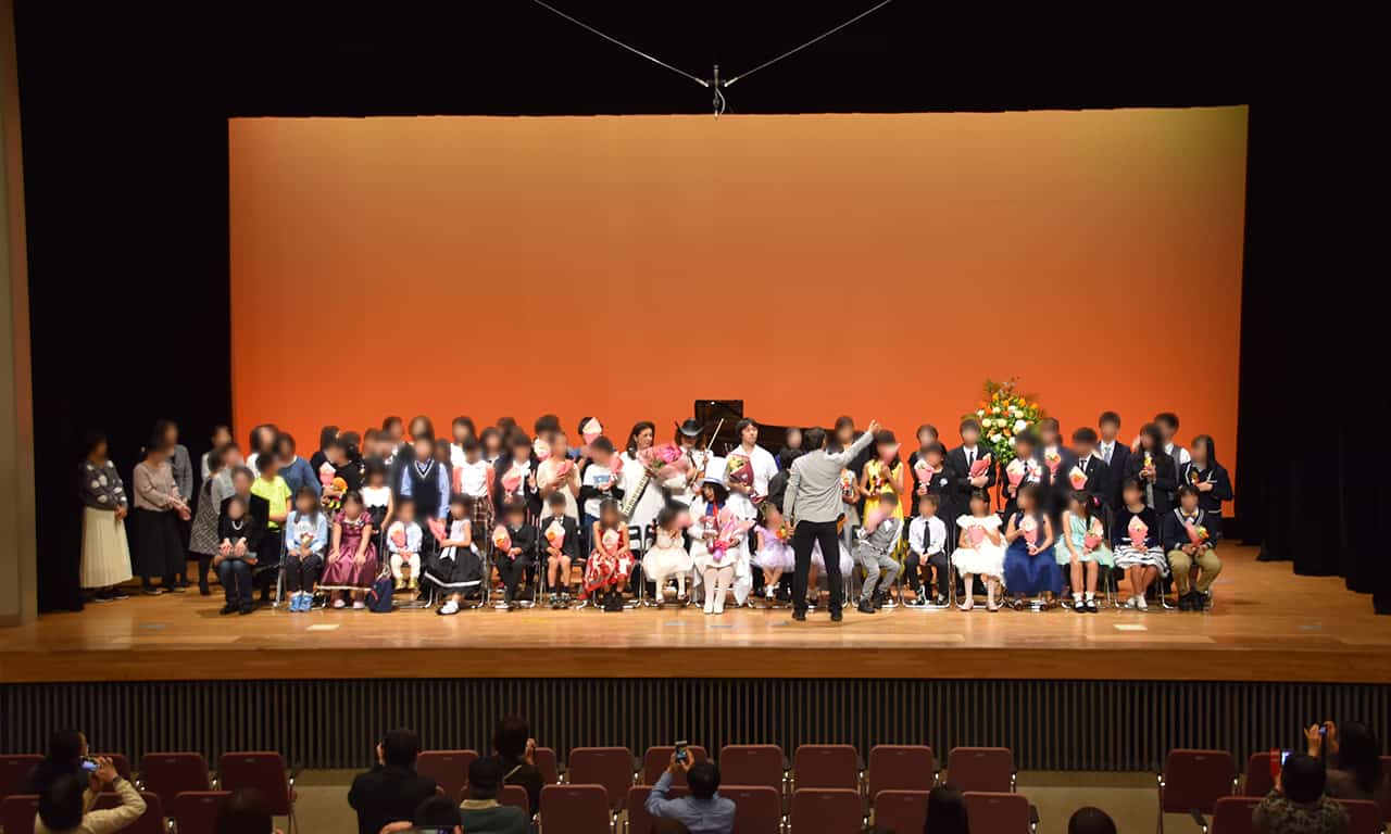 写真：ステージに並べられたイスに座っている出演者の前で、撮影のための指揮をしているカメラマンの様子