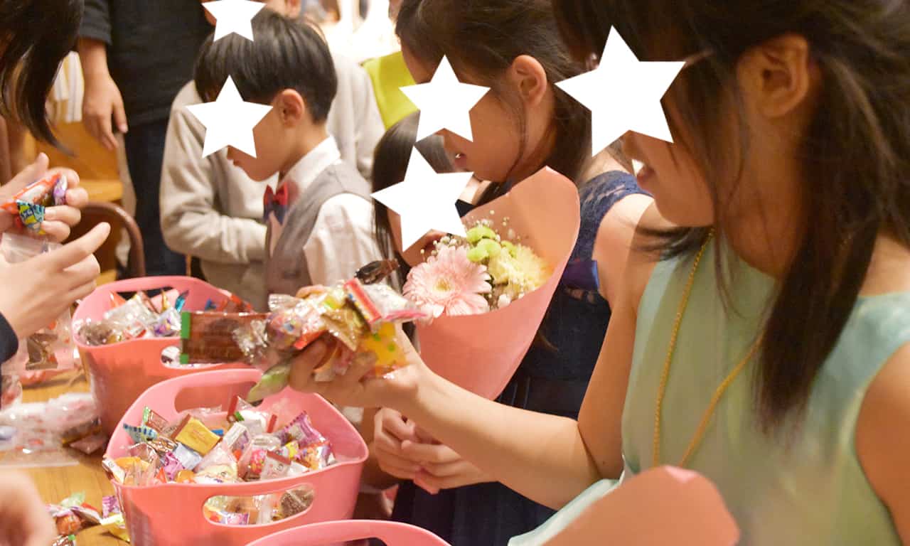 写真：3つの籠に山盛りになったアメ玉の前で順番に並び、片手でいっぱいのアメ玉を握りしめている子どもたち