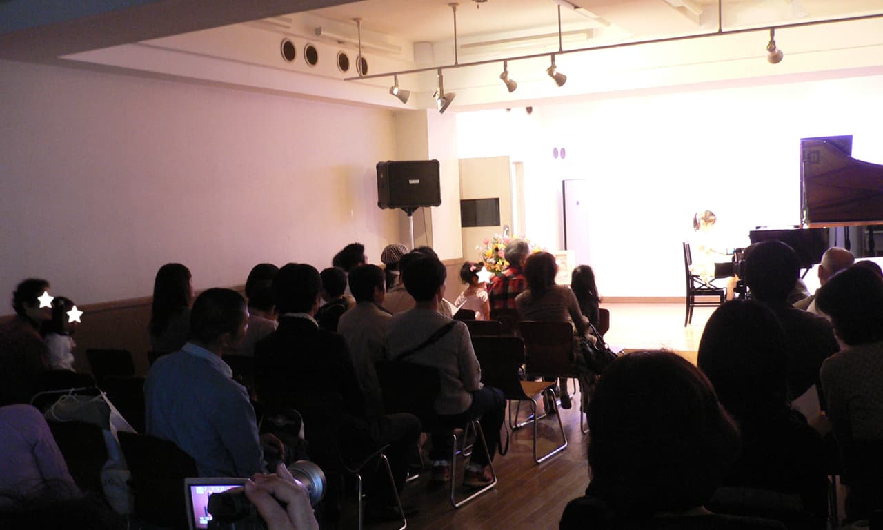 写真：たくさんの来場者の方々が見守る中、スポットライトが明るく照らすステージ上でピアノを演奏している女の子