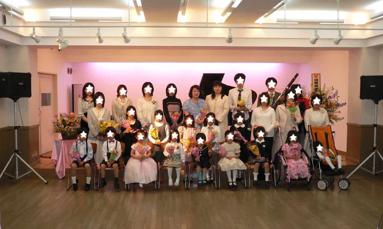 写真：ステージに集まって集合写真を撮っている出演の生徒さんと親御さん、ゲストの久松愛さん