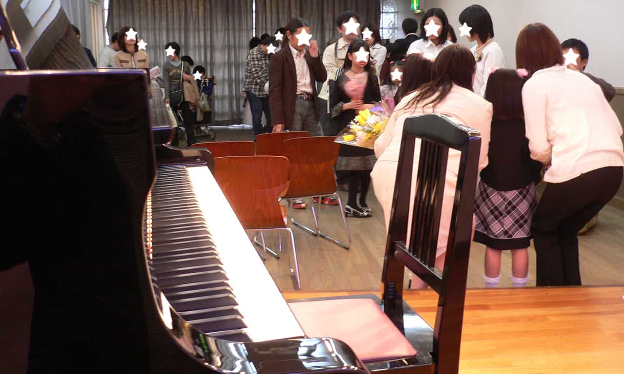 写真：ステージの前で講師と記念撮影する生徒と親御さん、そして順番待ちをしている方々