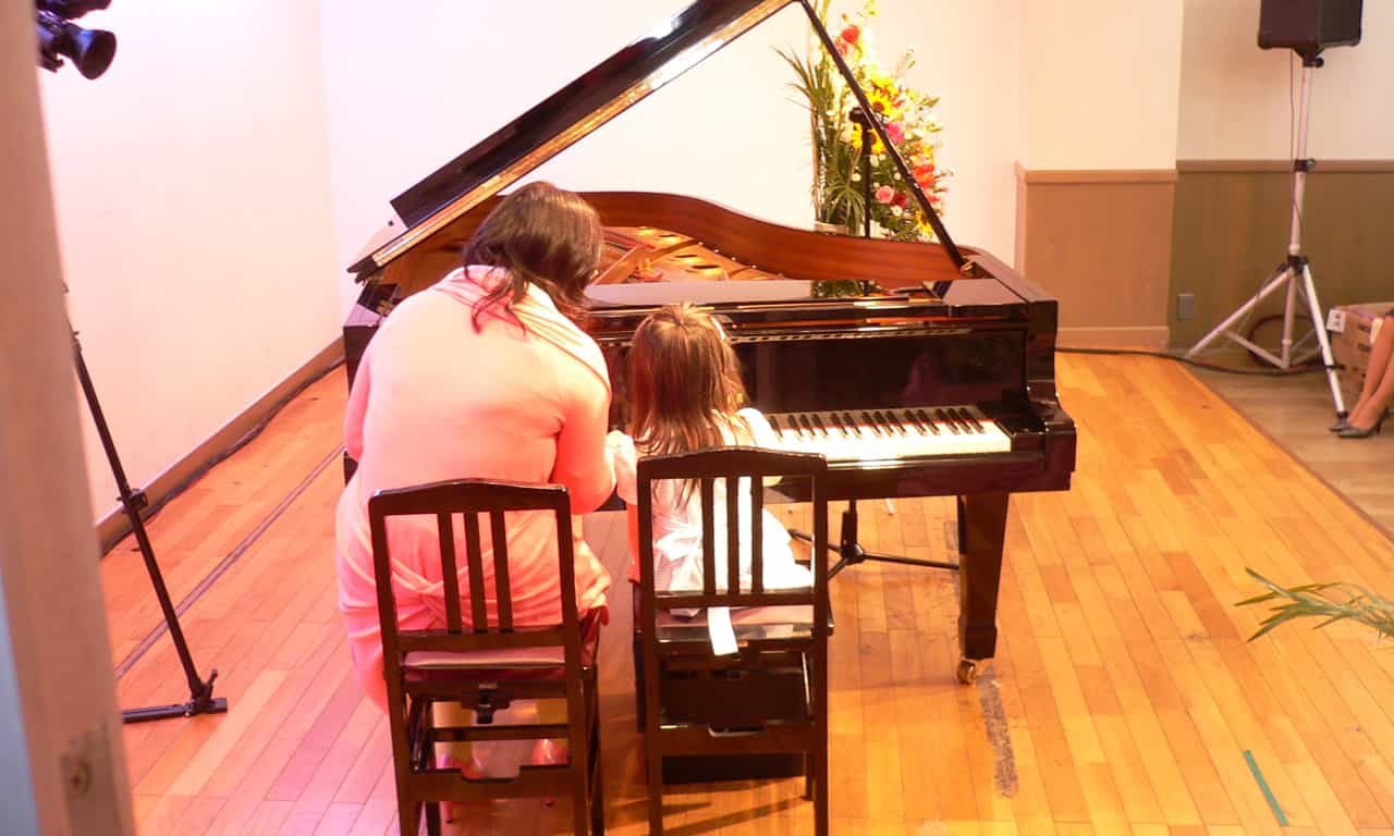 写真：講師と連弾する小さな女の子の後ろ姿