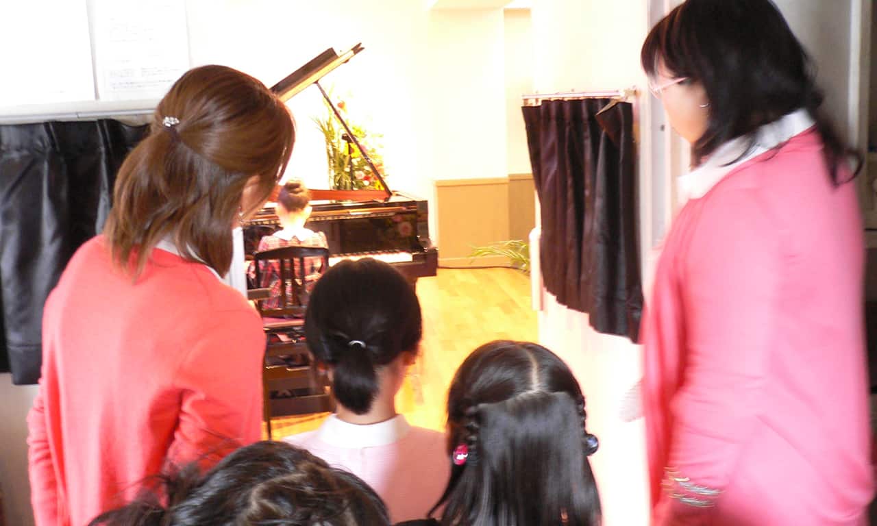 写真：ステージでピアノを弾いている女の子を見ながら、舞台袖に並び出番を舞っている子どもたち