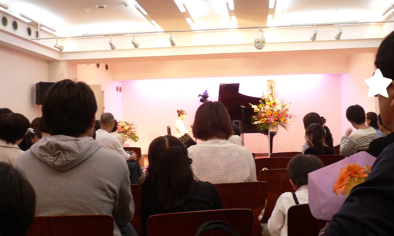 写真：客席後方から来場者越しに見える、ステージで演奏する女の子