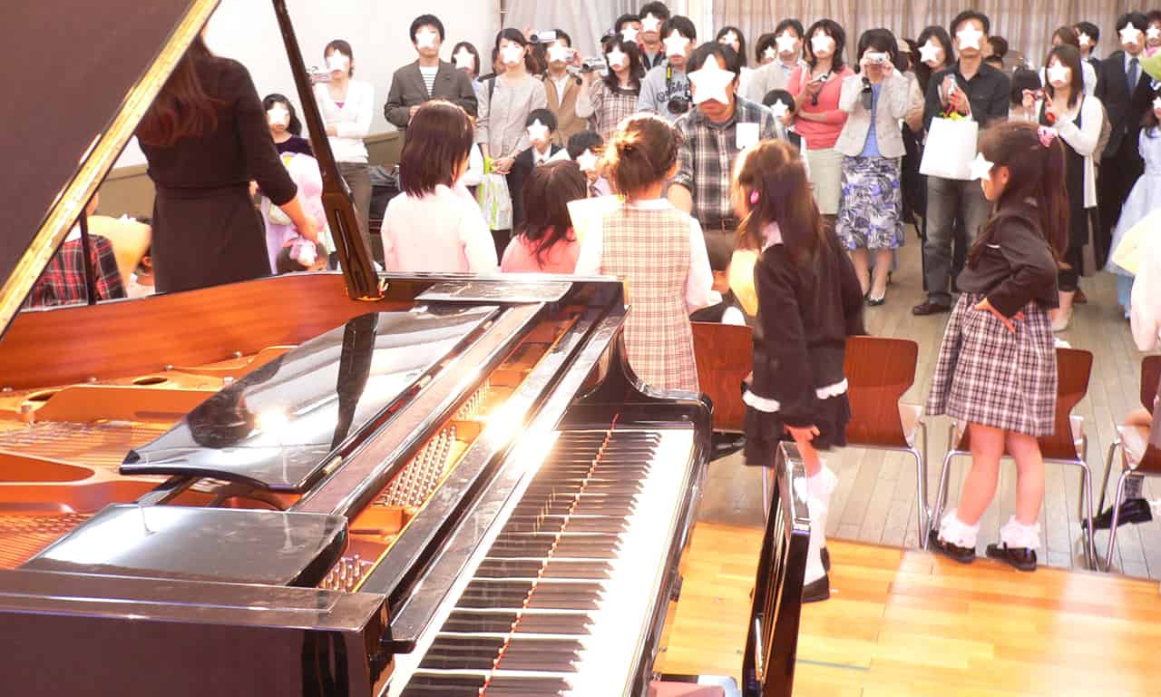 写真：ステージピアノ越しに見た、記念撮影にために整列している生徒さんたちの様子