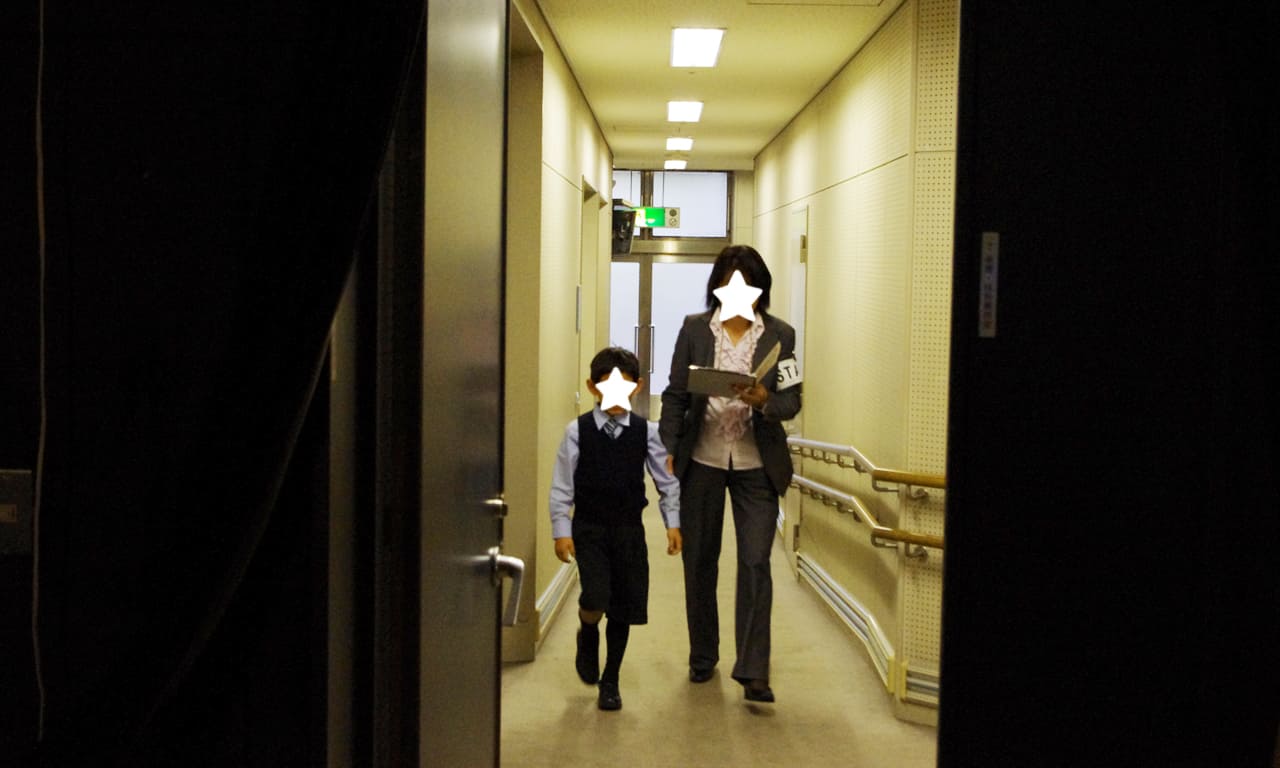 写真：楽屋から舞台袖へと向かう通路を歩いてくる男の子とスタッフ