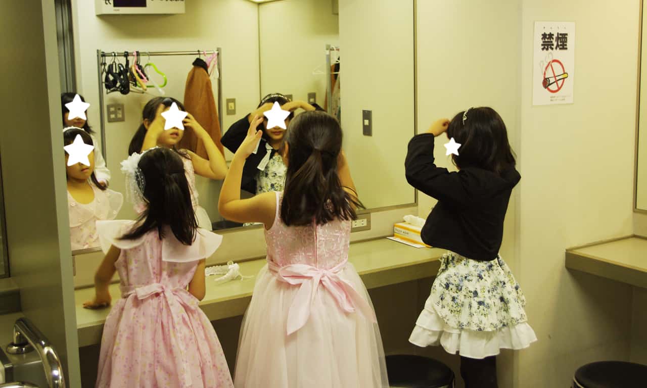 写真：楽屋の大きな鏡の前で髪型や衣装をチェックする4人の女の子たちの様子