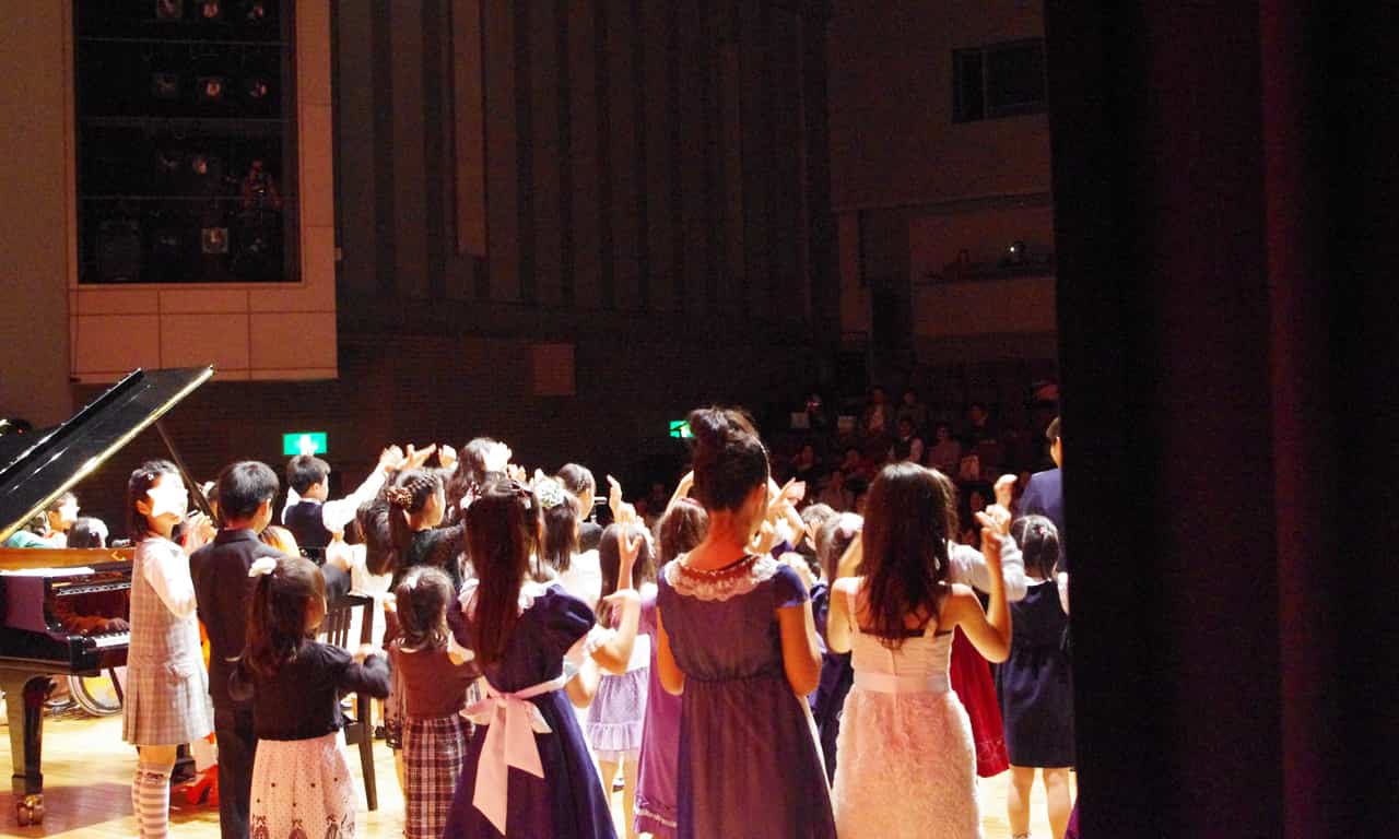 写真：ステージ上に集合して歌っている子どもたちを舞台袖から見た様子