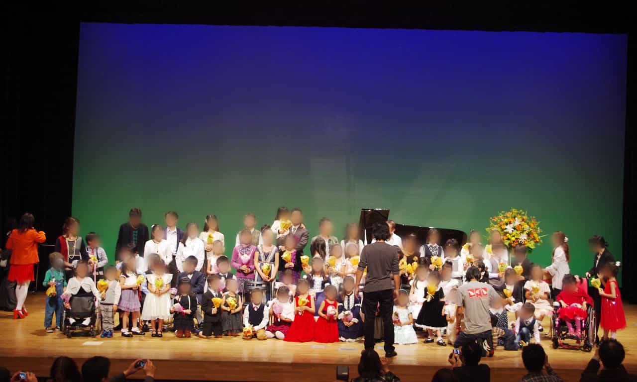 写真：カメラマンの指示で記念撮影のためにステージ上で綺麗に整列している生徒さんたち