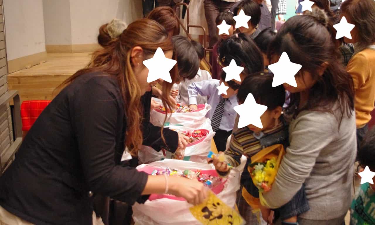 写真：舞台下に設けられたテーブルのカゴの中から、アメ玉をつかみ取る子どもたちの様子