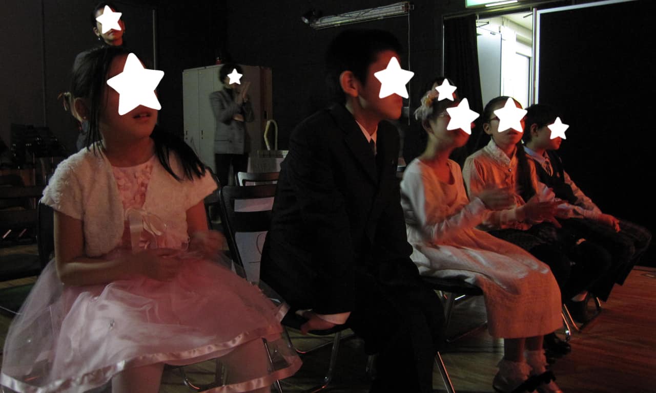 写真：舞台袖の待機椅子に座わりステージでの演奏に見入っている、出番待ちの子どもたちの様子