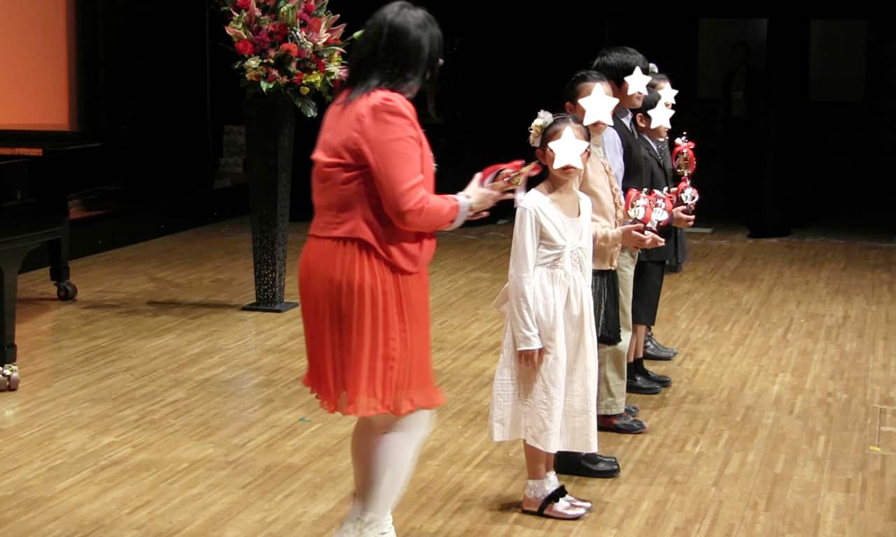 写真：ステージ上に横並びで整列し、講師からトロフィーを受け取っている、発表会5回出演賞受賞のみなさんの様子