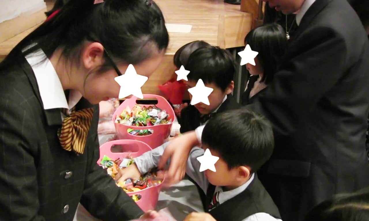 写真：カゴに山盛りのアメ玉を掴もうと手を伸ばす子どもたちの様子