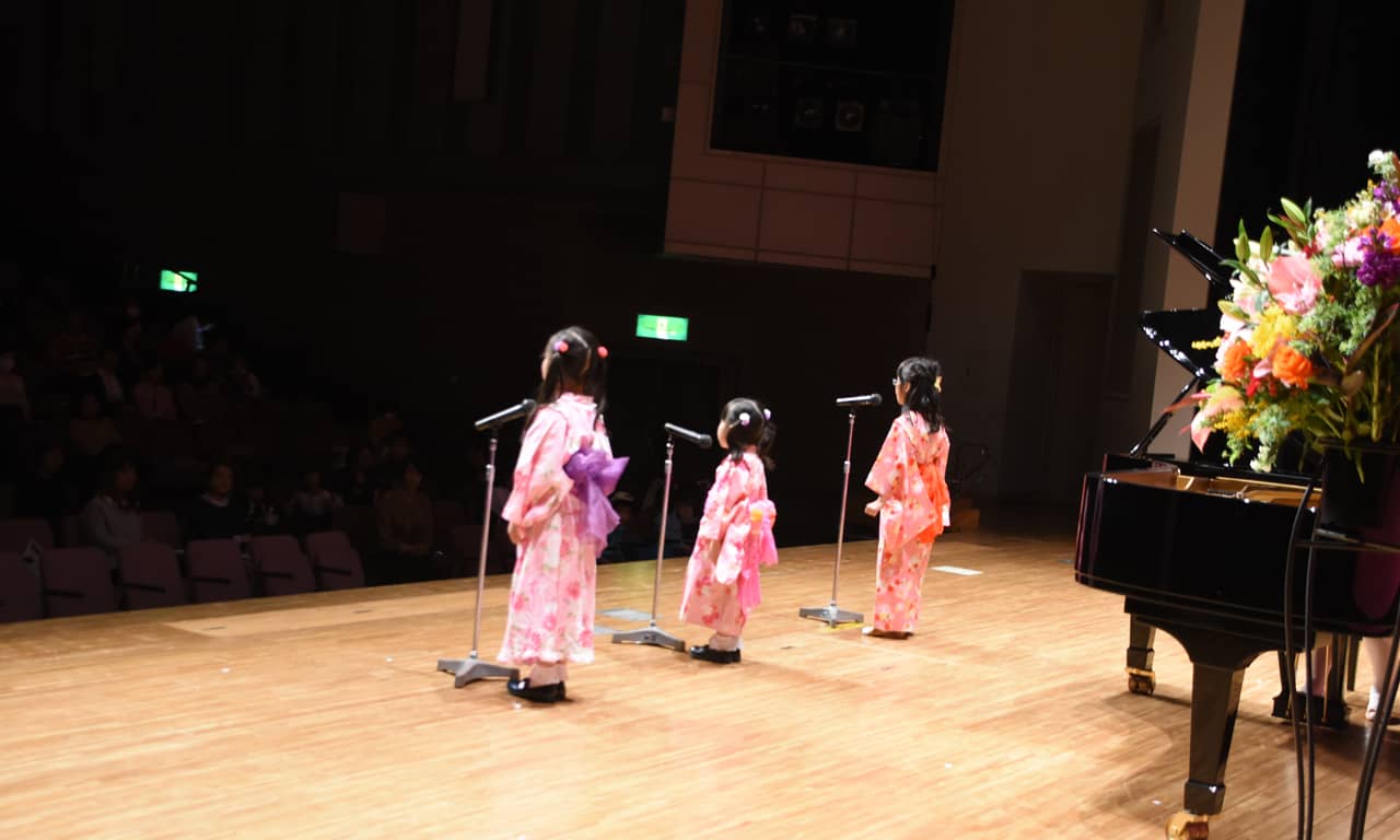 写真：浴衣姿の三人の女の子が客席に向かって歌っている舞台