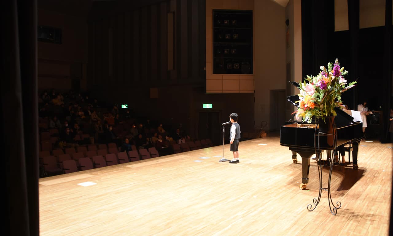 写真：大きなステージにひとり立ち、マイクに向かって堂々と歌う男の子