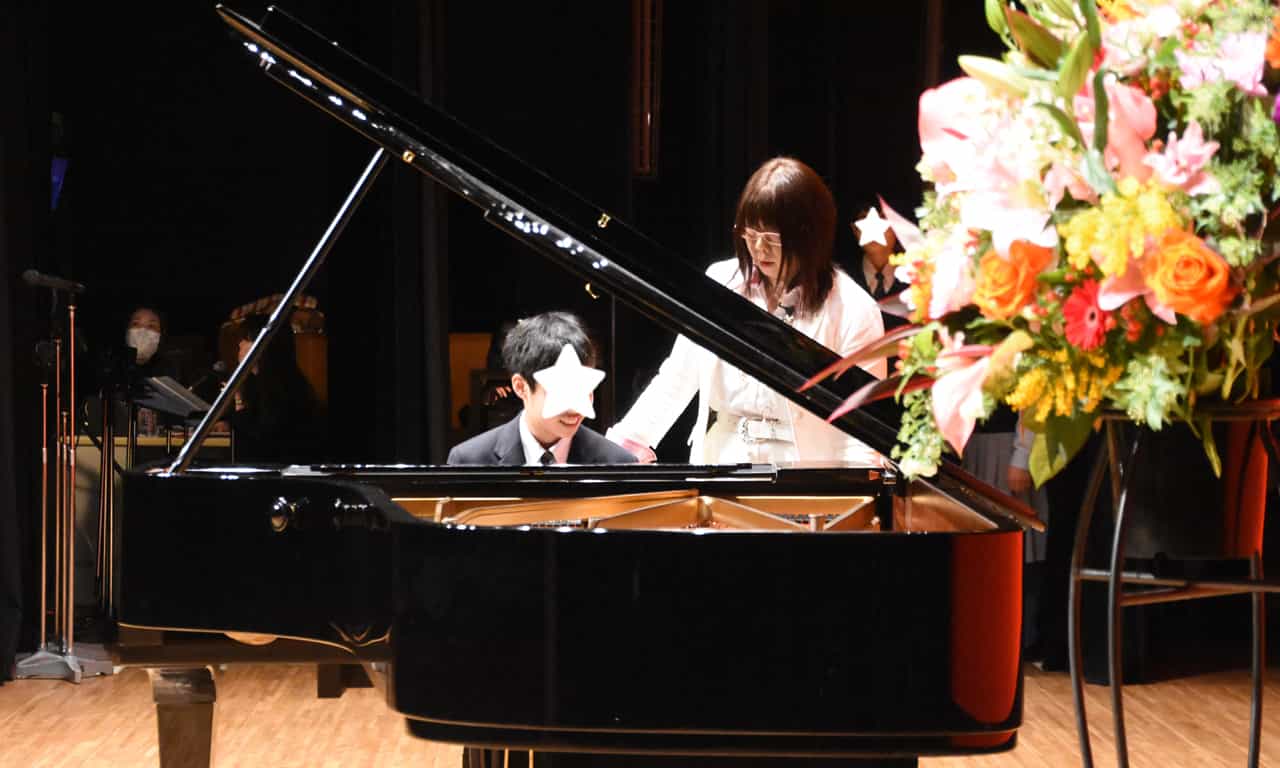 写真：ピアノに座って演奏開始直前、講師に声を掛けられている男の子