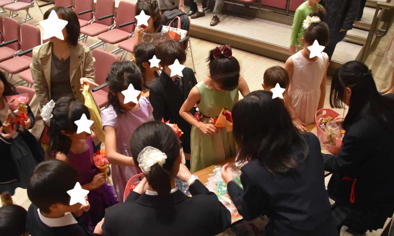 写真：会場出口に設けられたテーブルに並び、籠に入った山盛りのアメ玉を、手にひらいっぱいにつかんでいる子どもたちの、楽しそうな様子。